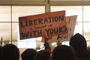 Protester's sign at DIA reads "My liberation is bound up with yours"