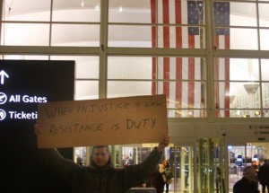 Protester's sign at DIA reads "When injustice is law, resistance is duty"